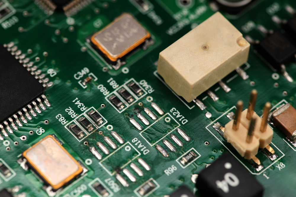 Close-up of an electronic circuit board highlighting a beige-colored Temperature Compensated Crystal Oscillator (TCXO) which ensures frequency stability of oscillators in electronic devices.