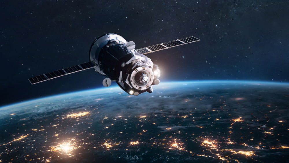 A satellite equipped with a Temperature Compensated Crystal Oscillator (TCXO) for precise timing, orbits Earth, its solar panels catching the sun's light against the contrasting city lights below.